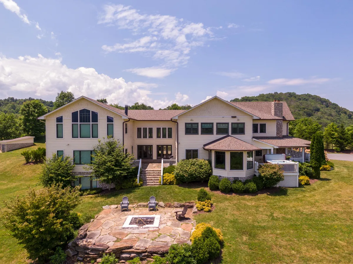 A cozy stone patio featuring a welcoming fire pit area with group seating, surrounded by greenery and views of the house. The scene suggests a perfect spot for evening gatherings, storytelling, and roasting s’mores under the sky.