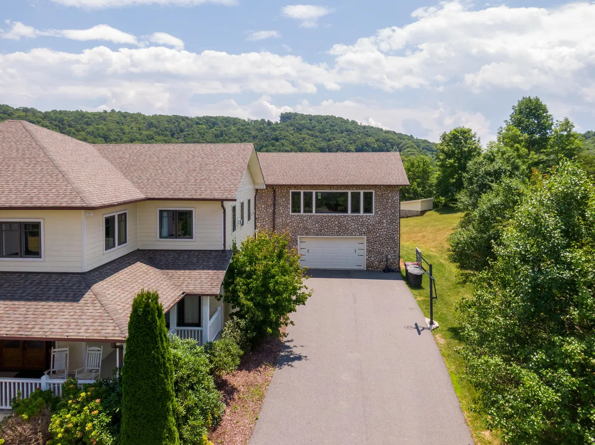 A wide view of the main house, garage, and spacious, level driveway bordered by manicured landscaping. The open area hints at room for team sports, snow tubing, or play, and showcases the scale of the property within its natural setting.