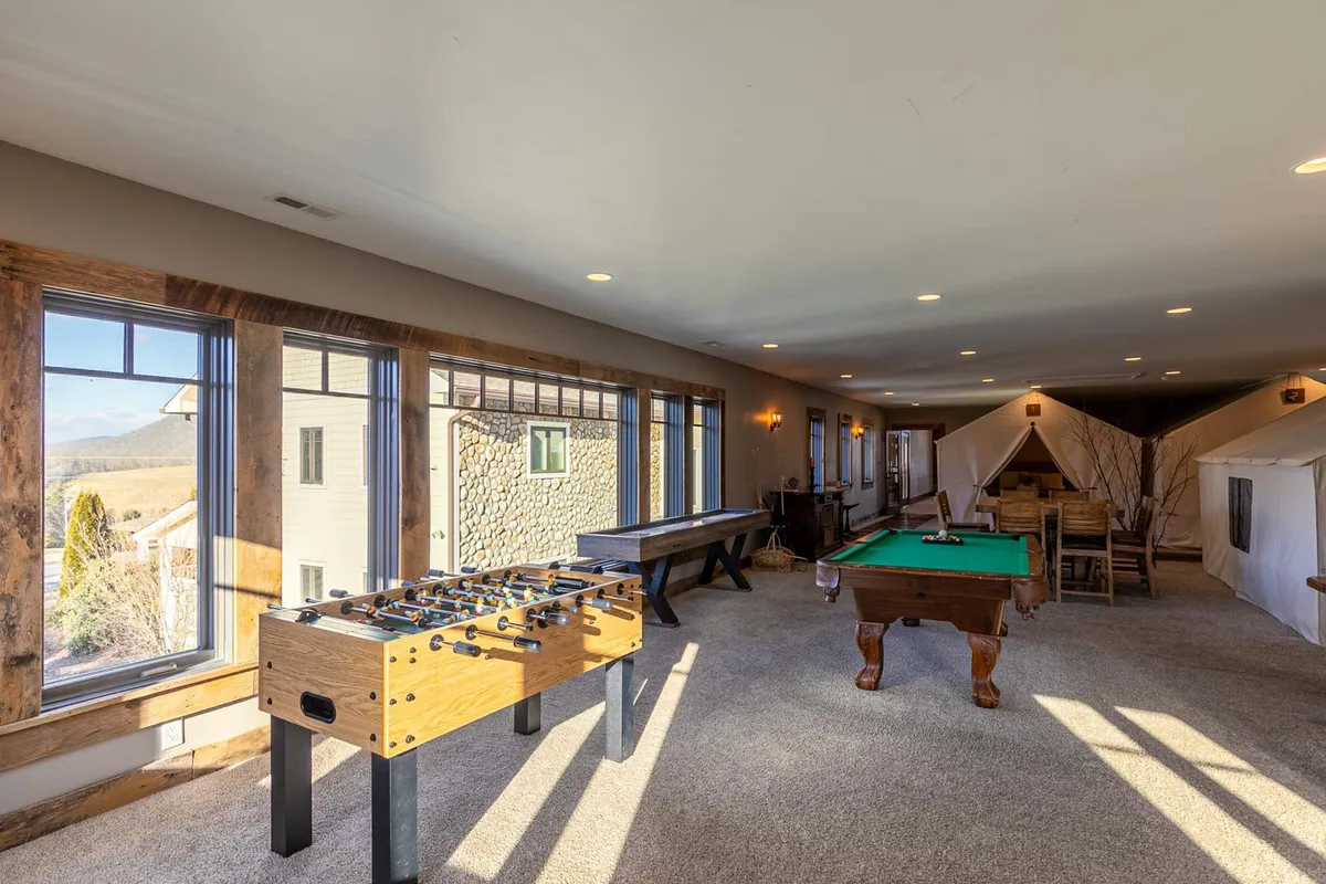 A vibrant scene with foosball and pool tables, tent-like structures in the background, and guests enjoying games together in a playful, casual atmosphere. The presence of tents and game tables highlights both the adventurous and entertainment aspects of the space.