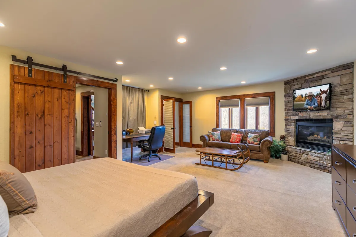 A spacious bedroom featuring a comfortable bed, a cozy fireplace, a plush sofa, and a desk. The room is illuminated by natural light, with inviting decor and a welcoming atmosphere that encourages relaxation.