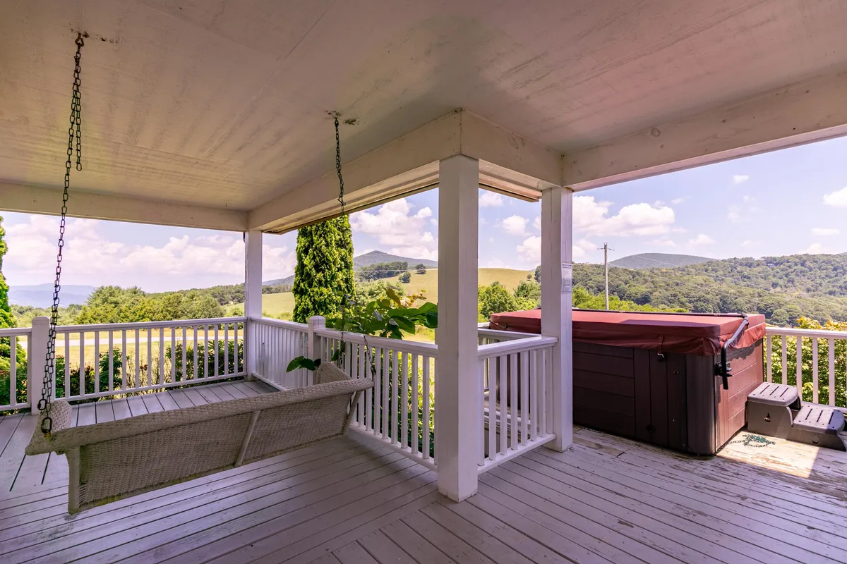 A swinging bench and a generously sized hot tub grace a covered porch, with panoramic mountain views in the background. This tranquil exterior highlights relaxation opportunities after a day of outdoor activity, whether soaking sore muscles or sharing drinks with friends.