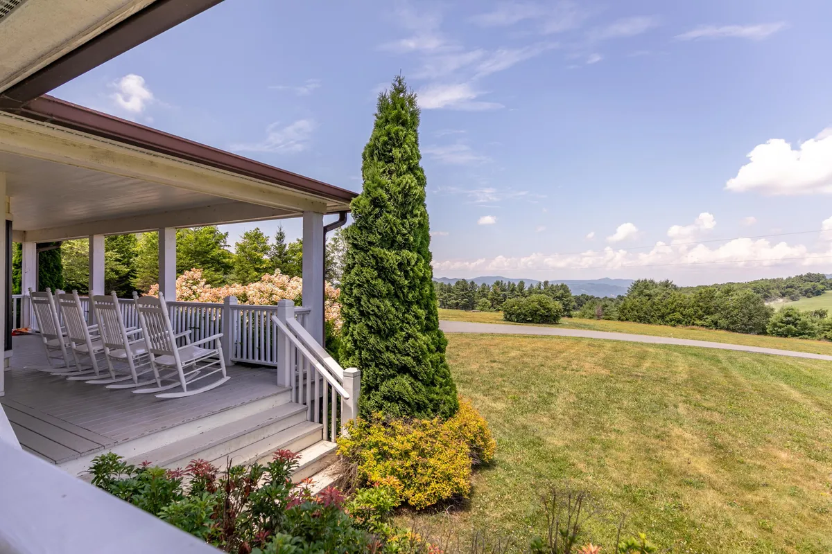 A charming front porch outfitted with classic rocking chairs overlooking green shrubbery and gentle hills in the distance. The scene evokes peaceful moments of relaxation, conversation, or stargazing from the comfort of the porch.
