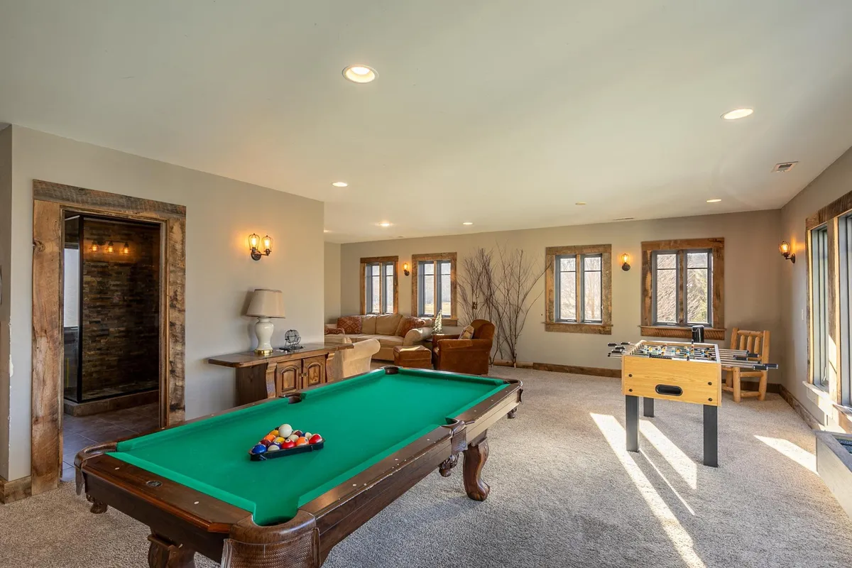 This view centers around a pool table and foosball table in a comfortable seating area, with large windows letting in natural light. The arrangement speaks to a welcoming environment for both games and relaxation, reinforcing the room’s function as a communal adventure space.