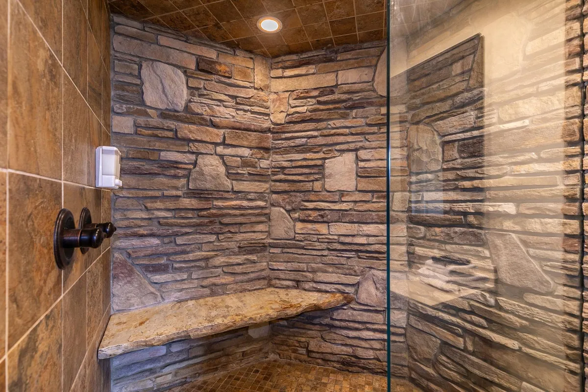A spa-inspired bathroom featuring textured stone walls, a glass shower enclosure, and a natural stone bench. The ambiance is calm and rejuvenating, evoking a spa-like experience.